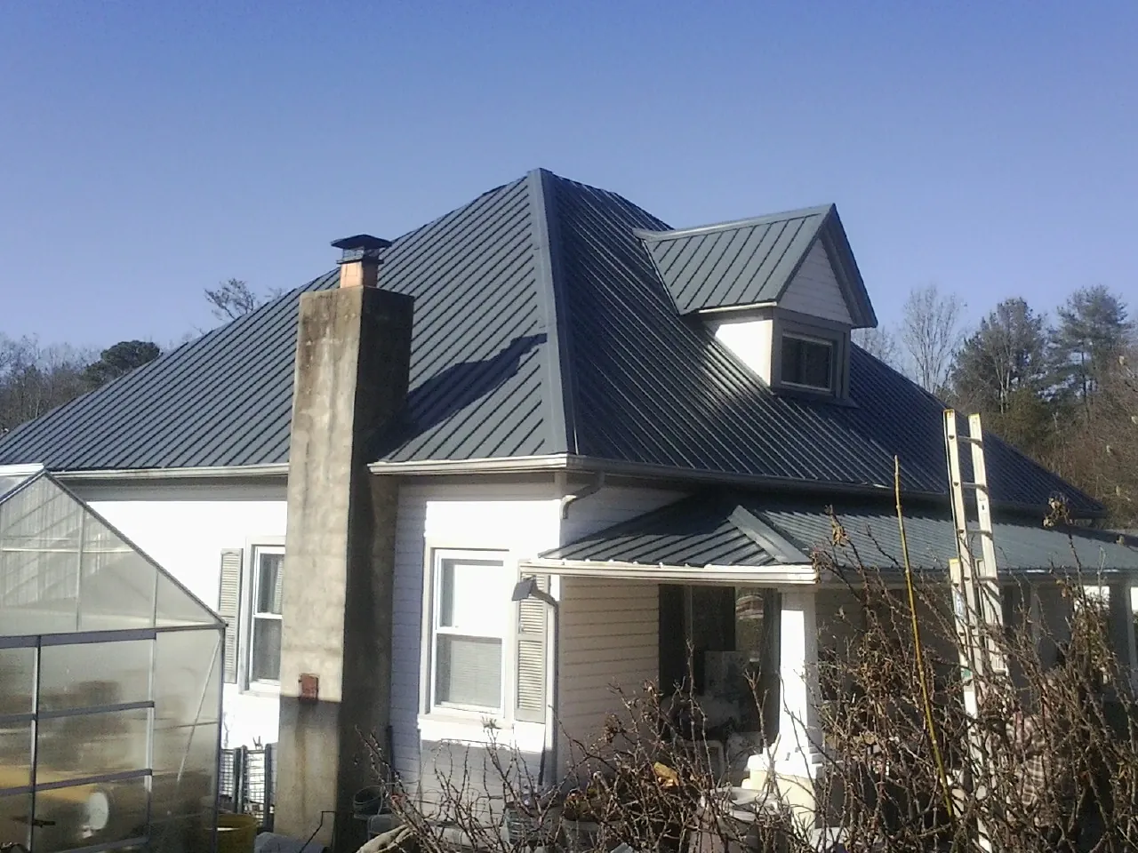 Dark blue standing seam metal roof on a white farmhouse with dormer — Slate & Tile Roof Repair by Roofing Brothers in Romeo