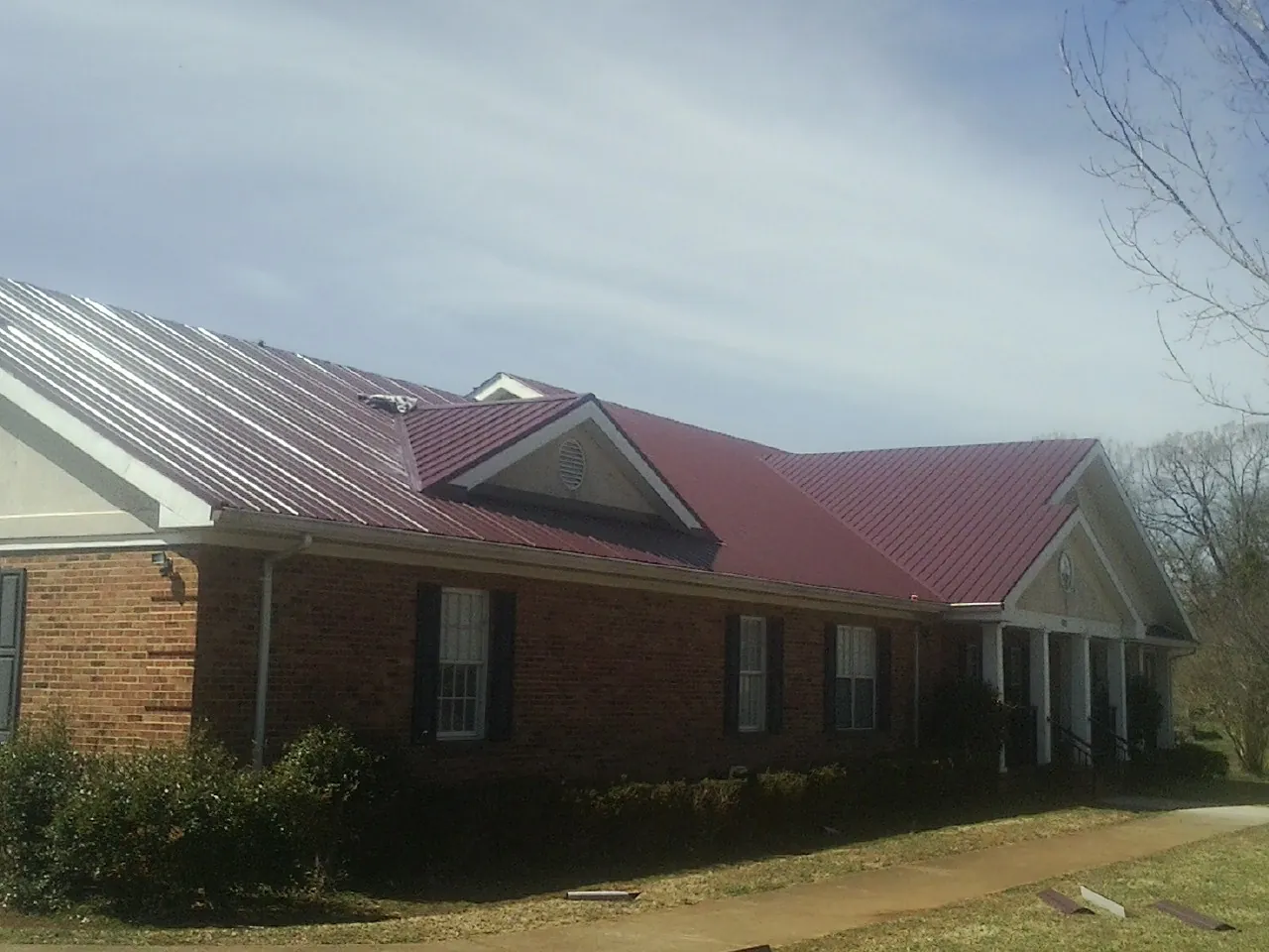 Red metal roof with gabled entries on a long brick building, from a Hail Damage Roof Repair job in Romeo