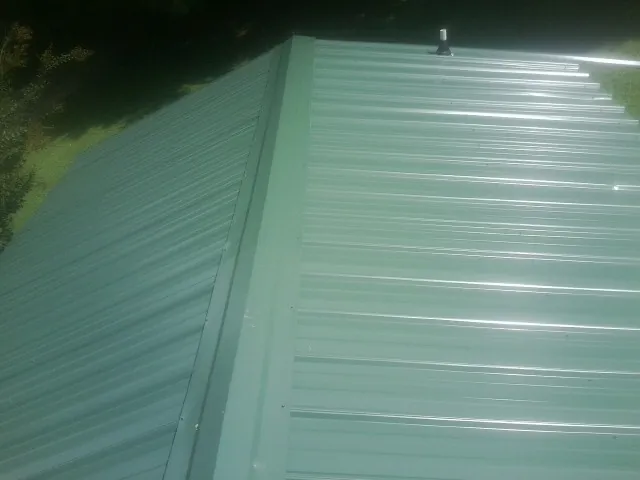 New green metal panels meeting at the ridge of a roof — Flat Roof Repair work by our crew in Romeo