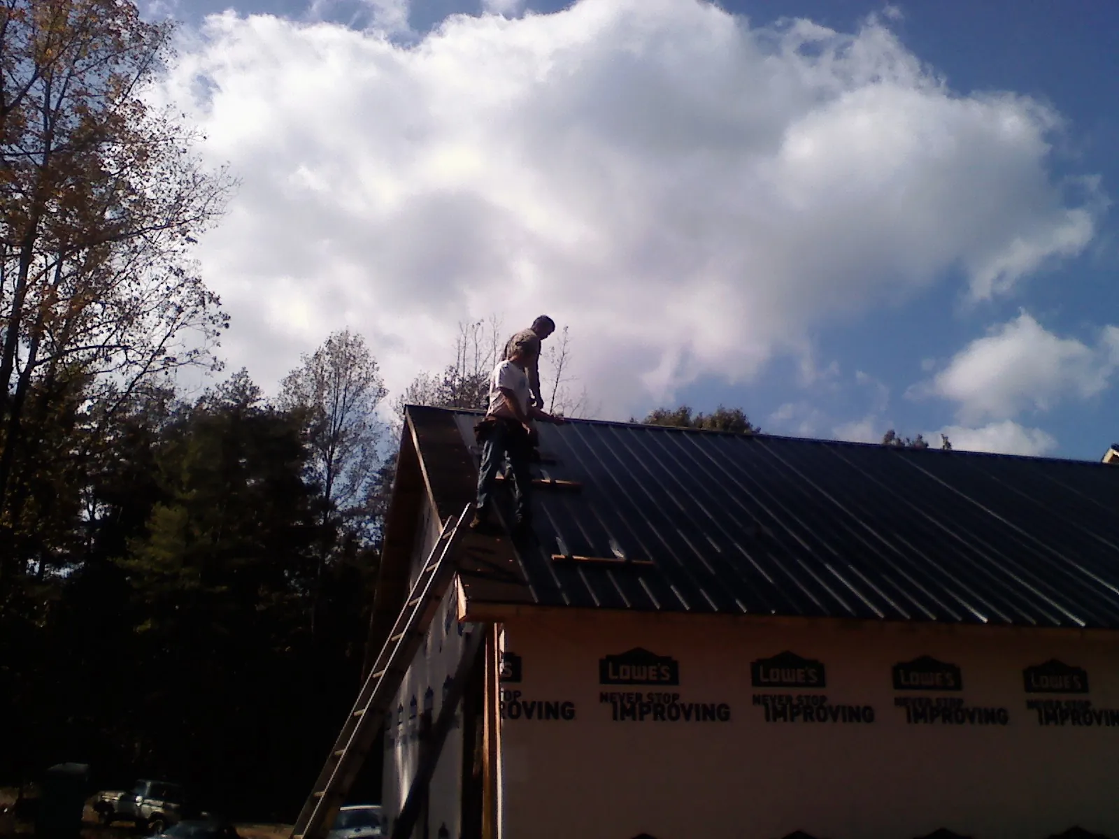 Roofer fastening dark metal panels high against a cloudy sky, from a Roof Inspection job in Romeo