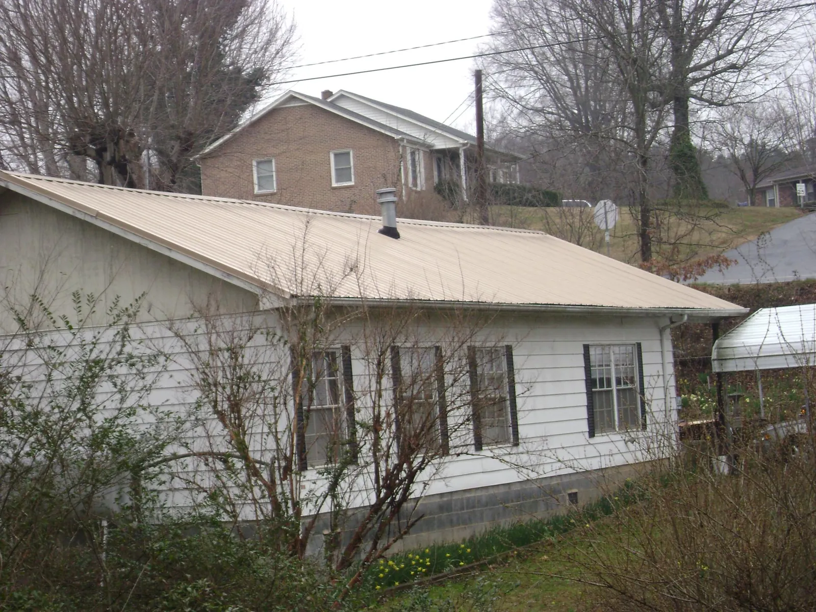 Tan metal roof on a white sided house set into a hillside — Commercial Roofing by Roofing Brothers in Romeo